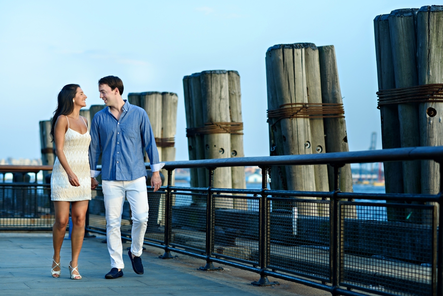 An engaged couple walking along the hudson river and laughing during their engagement session.